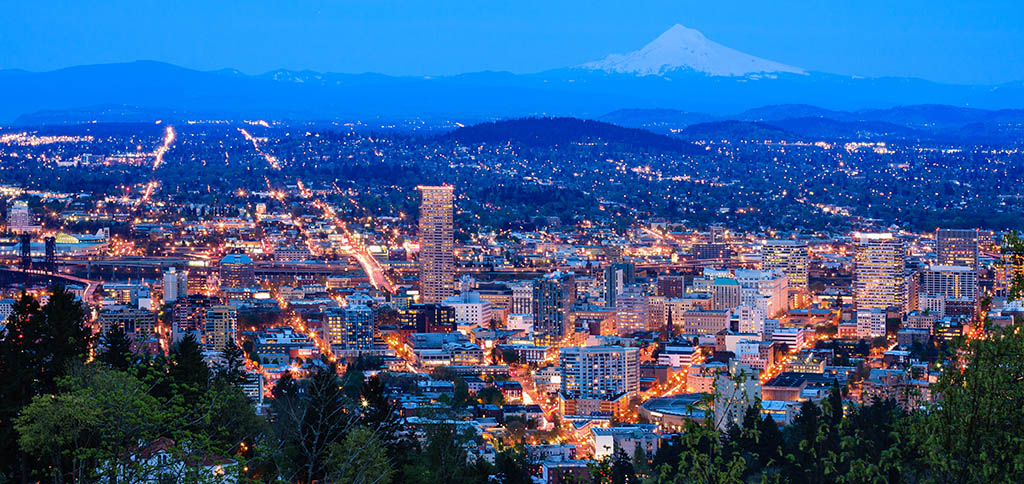 Portland Oregon metro glows with light at dusk while Mount Hood watches over