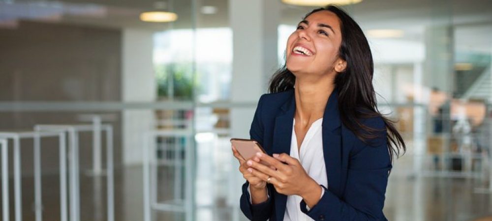 Excited businesswoman using smartphone. Beautiful happy young woman in formal wear using mobile phone and laughing. Technology concept